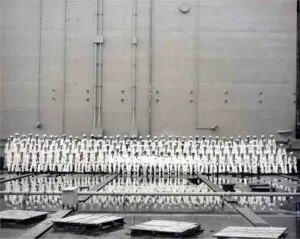Sailors in uniform stand in formation before a large ship hull, possibly an ABSD.