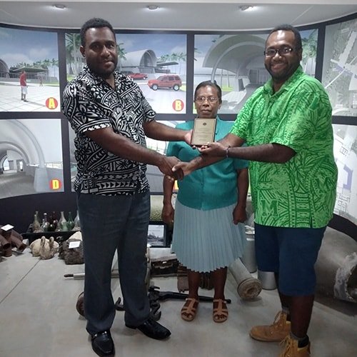 Men present a plaque to a woman in front of architectural renderings