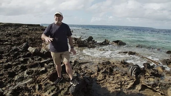 Man standing on rocky shore with wreckage near the ocean