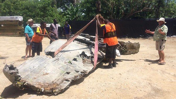 Airplane wreckage being lifted by crane with men watching