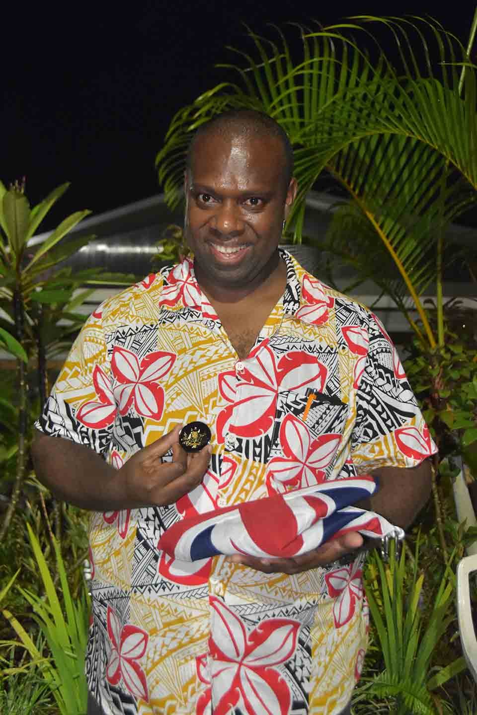 Man in a floral shirt holds a coin and a folded flag