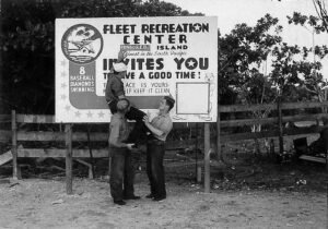 Fleet Recreation Center sign on Aore Island, with three men posing.