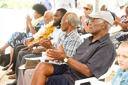 Elders in traditional attire clapping at a museum opening event.