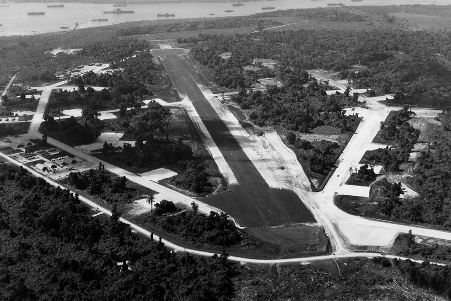 Aerial view of a WWII airfield with runways and surrounding jungle.