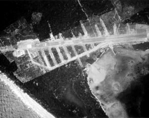 Aerial view of a WWII bomber airfield with rows of aircraft and jungle surroundings.