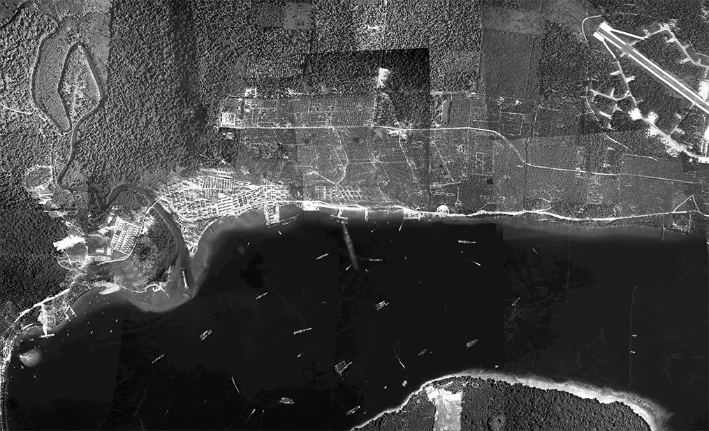 Aerial view of a naval base with ships in the harbor and an airfield