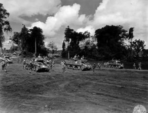 WWII Sherman tanks and soldiers training in a jungle clearing.
