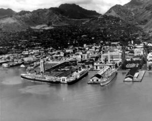 Aerial view of the Coolidge ship docked at a busy harbor with mountains behind.