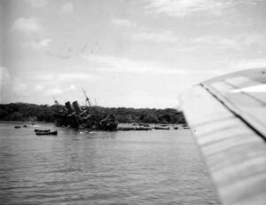 Wrecked USS Coolidge ship listing in shallow water, with smaller boats nearby