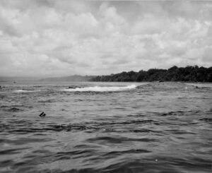 USS Coolidge shipwreck breaking the surface in calm waters near a lush, tree-lined shore.
