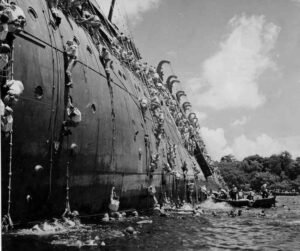 USS Coolidge crew climbing ropes from capsized ship during WWII.