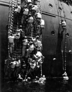 US Navy sailors climb a cargo net aboard the USS Coolidge during WWII.