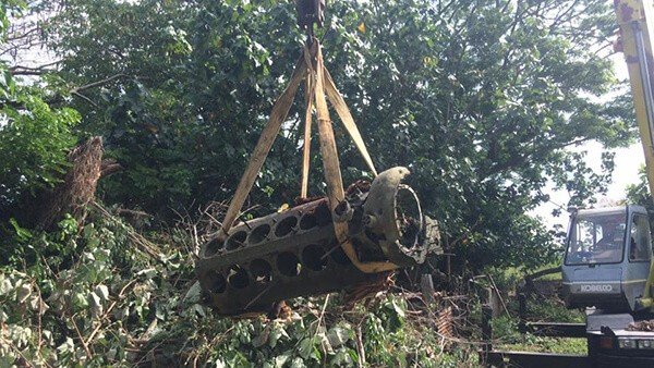 Crane lifting vintage aircraft engine from dense foliage