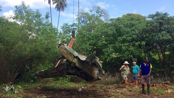 Aircraft wreckage being lifted by a crane with people watching