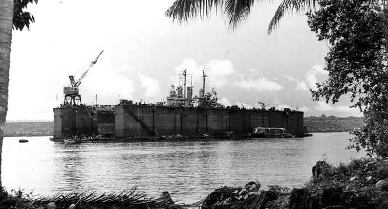 Floating dry dock with a ship inside, showing crane and palm trees.