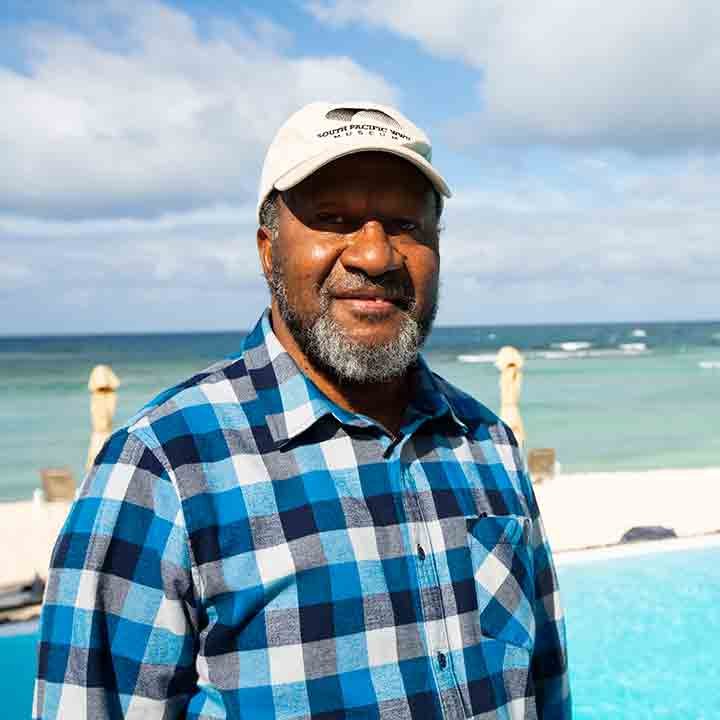 Man in a plaid shirt and baseball cap by the ocean