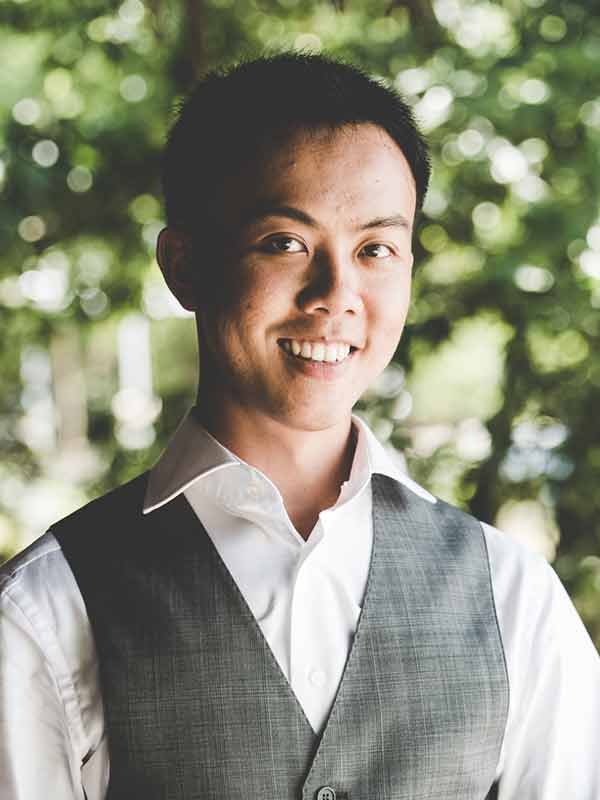 Museum team member, a young man in a vest and white shirt, smiles outdoors.