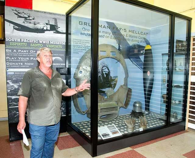 Man gestures at Grumman F6F Hellcat display at South Pacific WWII Museum, Vanuatu