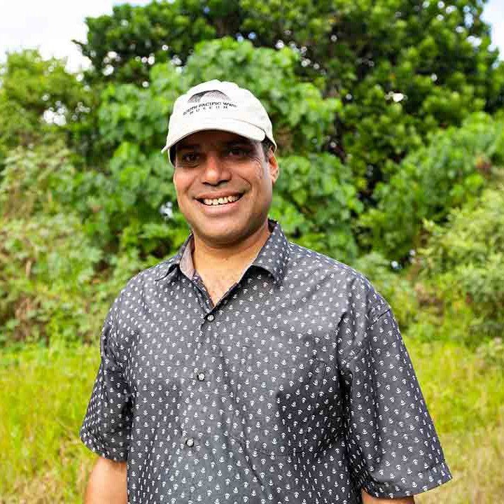 PM Foreign Minister filming outdoors, smiling in a cap and patterned shirt.