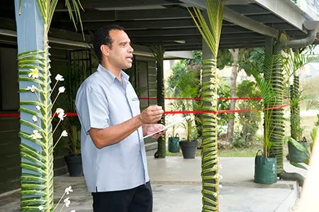 Man speaking at museum opening event, decorated with palm fronds.