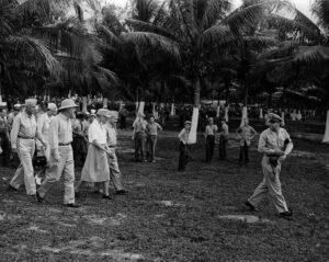 WWII military leaders walk under palm trees, possibly related to Roosevelt.