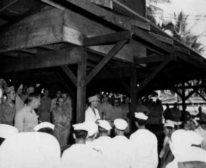 WWII troops gathered under a wooden structure, possibly a historical Roosevelt event.