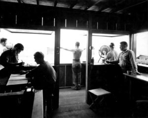 Men in a signal station, one signaling with arms outstretched.