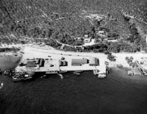 Aerial view of a historical military base with buildings, vehicles, and boats.