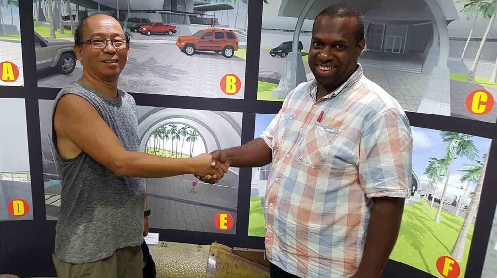Two men shaking hands in front of architectural renderings, one man wearing glasses.