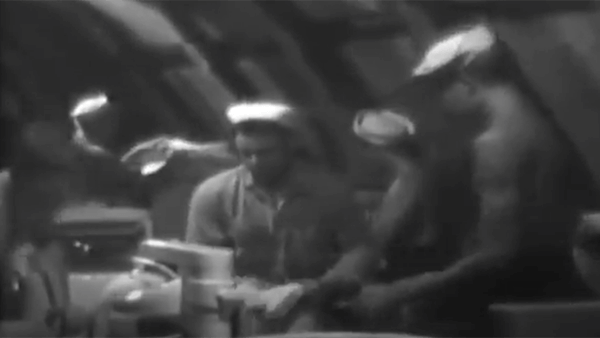 Men in a kitchen preparing food in a black and white video.