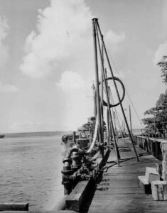 Ships docked at a historical wharf with industrial pumping equipment on a wooden pier.