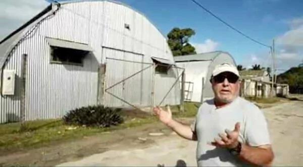 Man in front of a corrugated metal building, possibly a warehouse or barn.