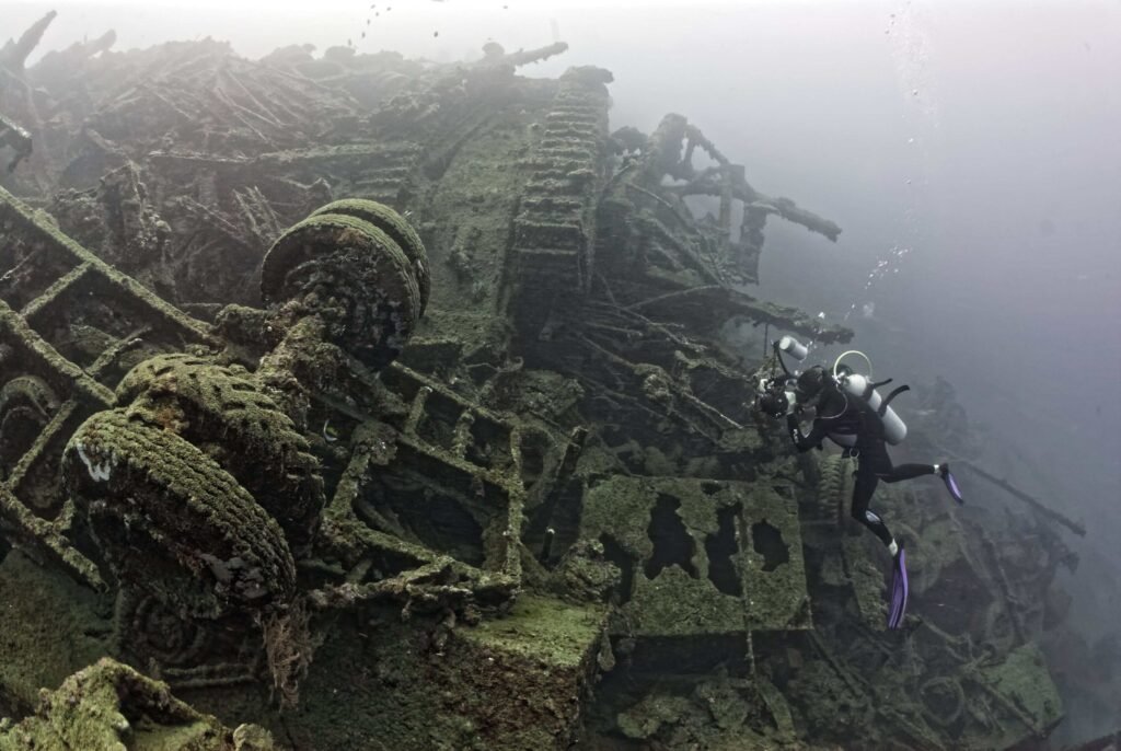 Scuba diver explores a sunken ship wreck, covered in marine growth.