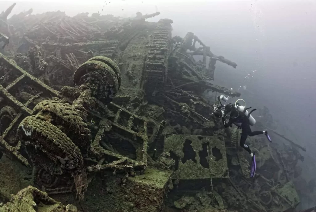 Scuba diver explores a sunken ship wreck, covered in marine growth.