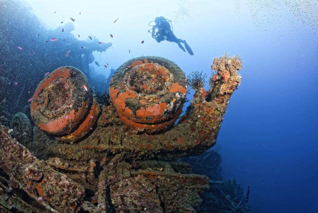Scuba diver explores a sunken ship's rusted machinery covered in marine life.
