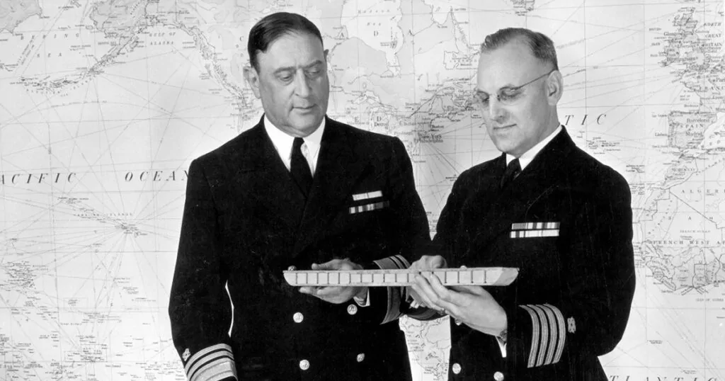 Two naval officers examine a model, floating an idea.