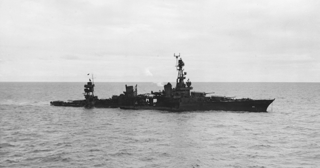 Damaged warship adrift at sea, possibly a cruiser or destroyer, with smoke rising.