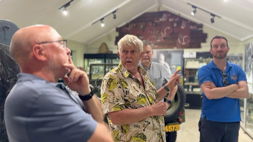 Tour group in a museum, one man gestures towards exhibits.