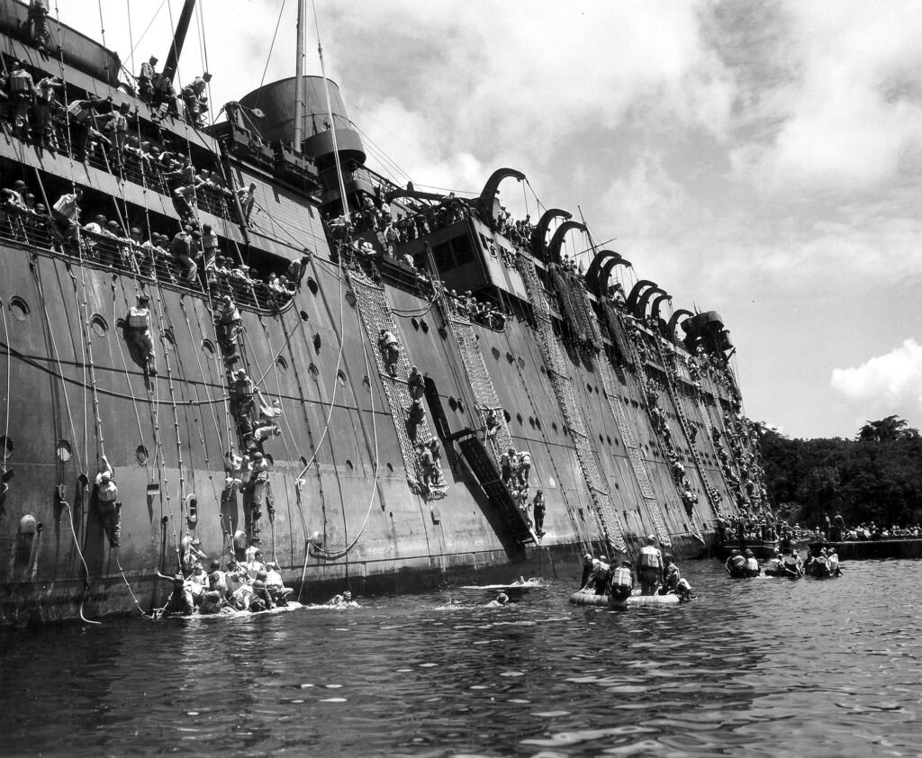 USS Coolidge passengers evacuate onto life rafts and nets during a wartime emergency.