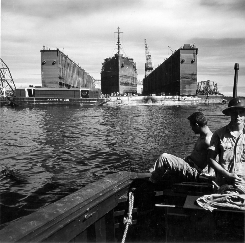Floating dry dock cradles a ship, with workers nearby.