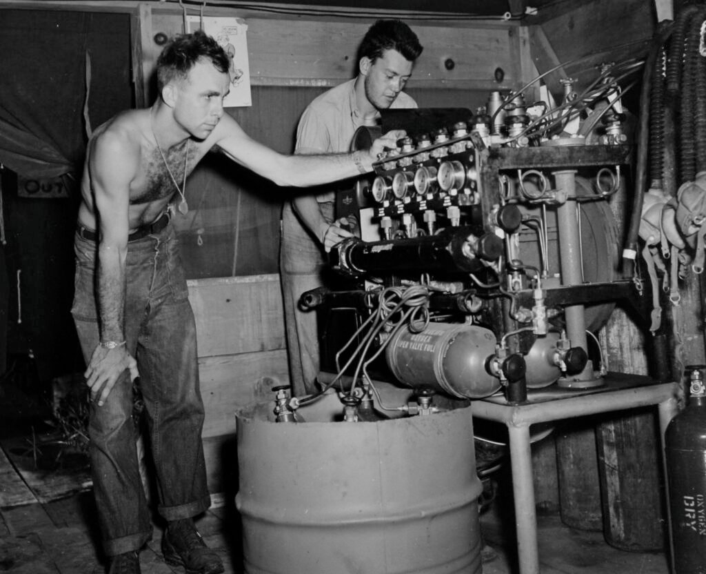 Two men work on complex machinery at an airfield.