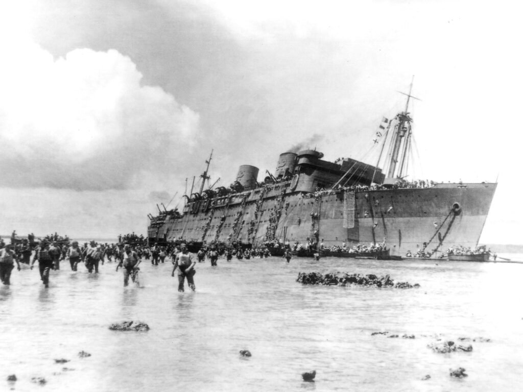 USS Coolidge evacuation: Soldiers wade ashore from a damaged ship.