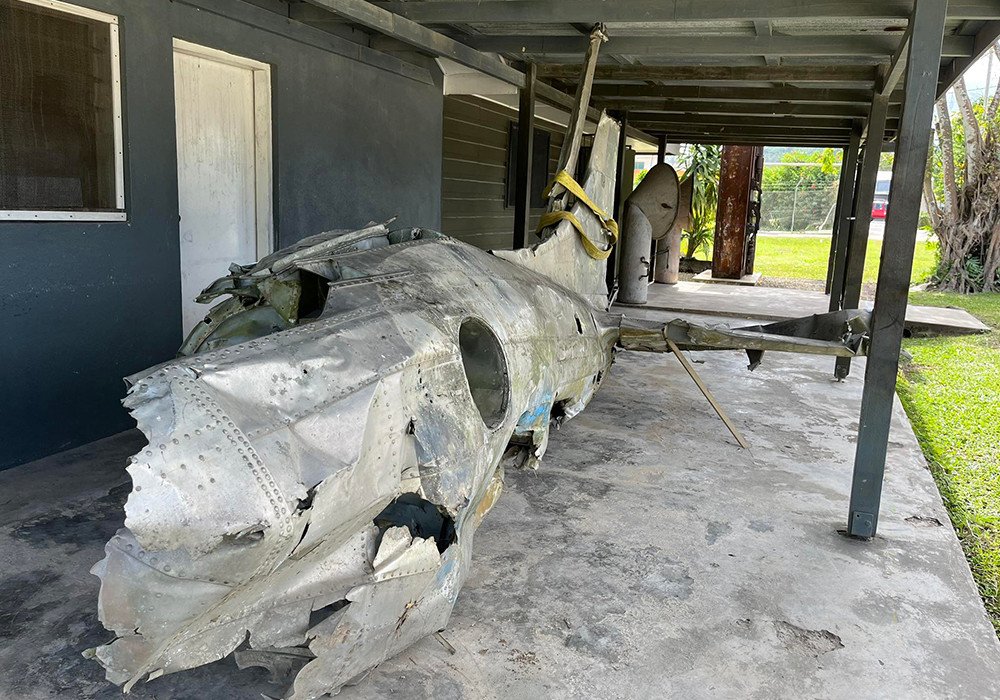 Damaged aircraft wreckage displayed under a covered walkway.