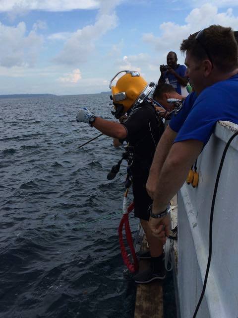 Commercial diver in yellow helmet prepares to enter the water from a boat.