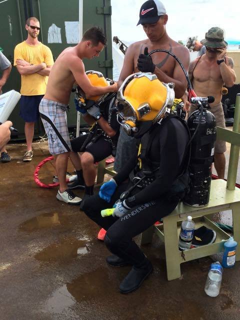 Divers prepare for a dive, with one in a yellow helmet and gear.