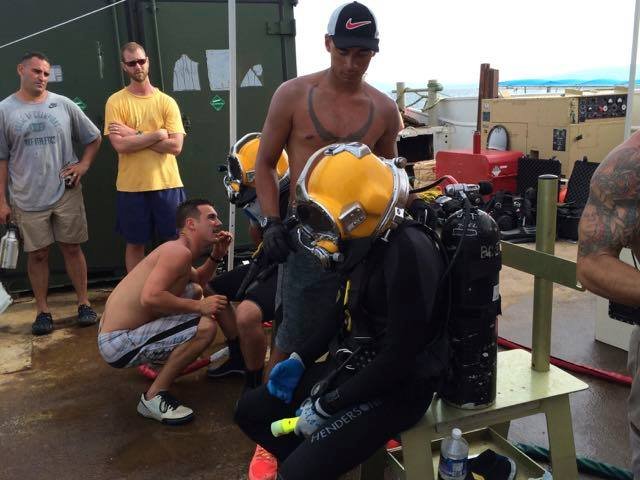 Divers in yellow helmets prepare equipment on a boat deck.