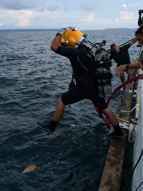 Commercial diver in yellow helmet jumps from boat into the ocean.