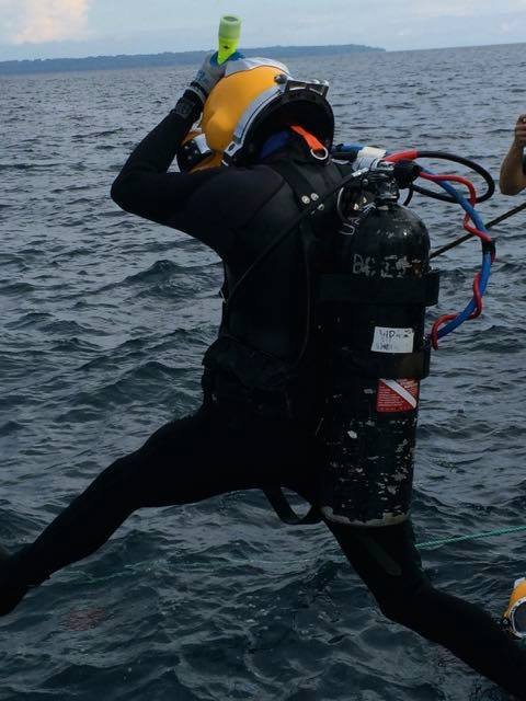 Commercial diver in helmet and wetsuit preparing to enter water.