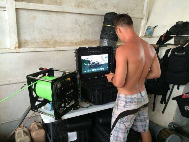 Man operating underwater camera equipment on a boat