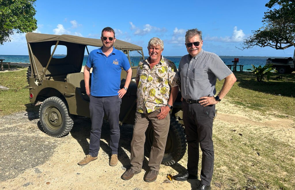 Three men with a vintage military jeep on a tropical beach.
